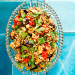 Bulgur salad with tomato and aubergine in transparent dish on turqoise tiles seen from above