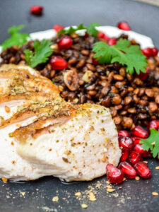 Chicken with Syrian lentils and labneh on a black plate, seen up close with chicken in focus