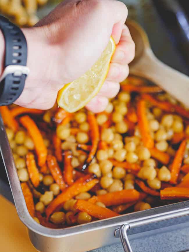 Hand squeezing lemon onto chickpeas and roast carrots