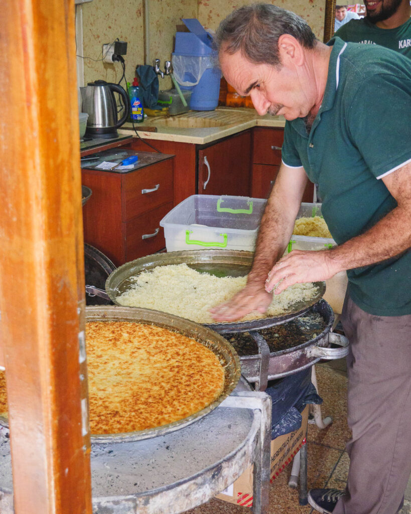A middle aged man makes künefe by pressing the kataif to the base of a large metal tray