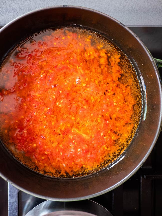 Grated tomato frying in oil in a pan, seen from above