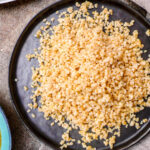Cooked coarse bulgur wheat on black plate, seen from above