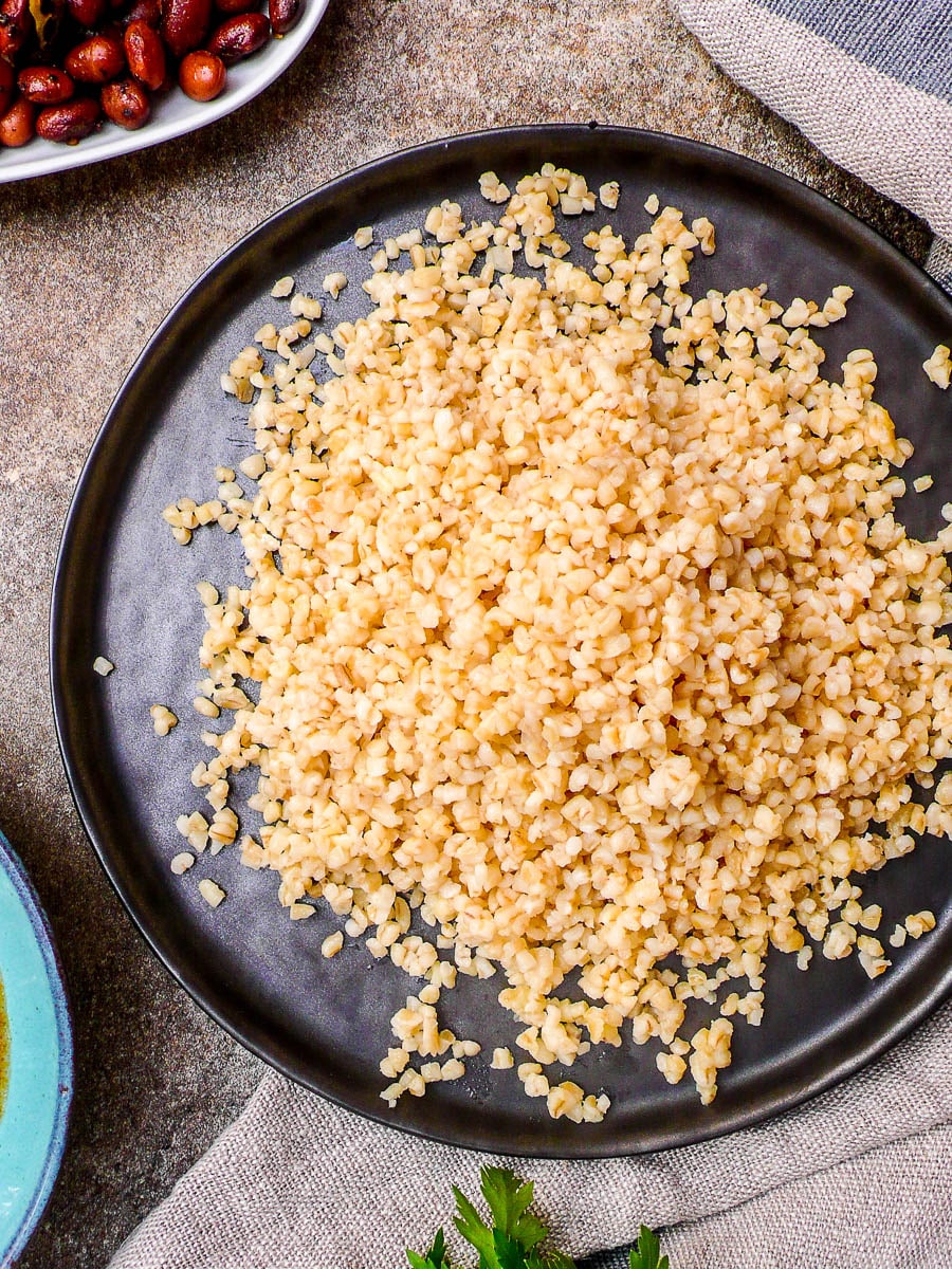 Cooked coarse bulgur wheat on black plate, seen from above