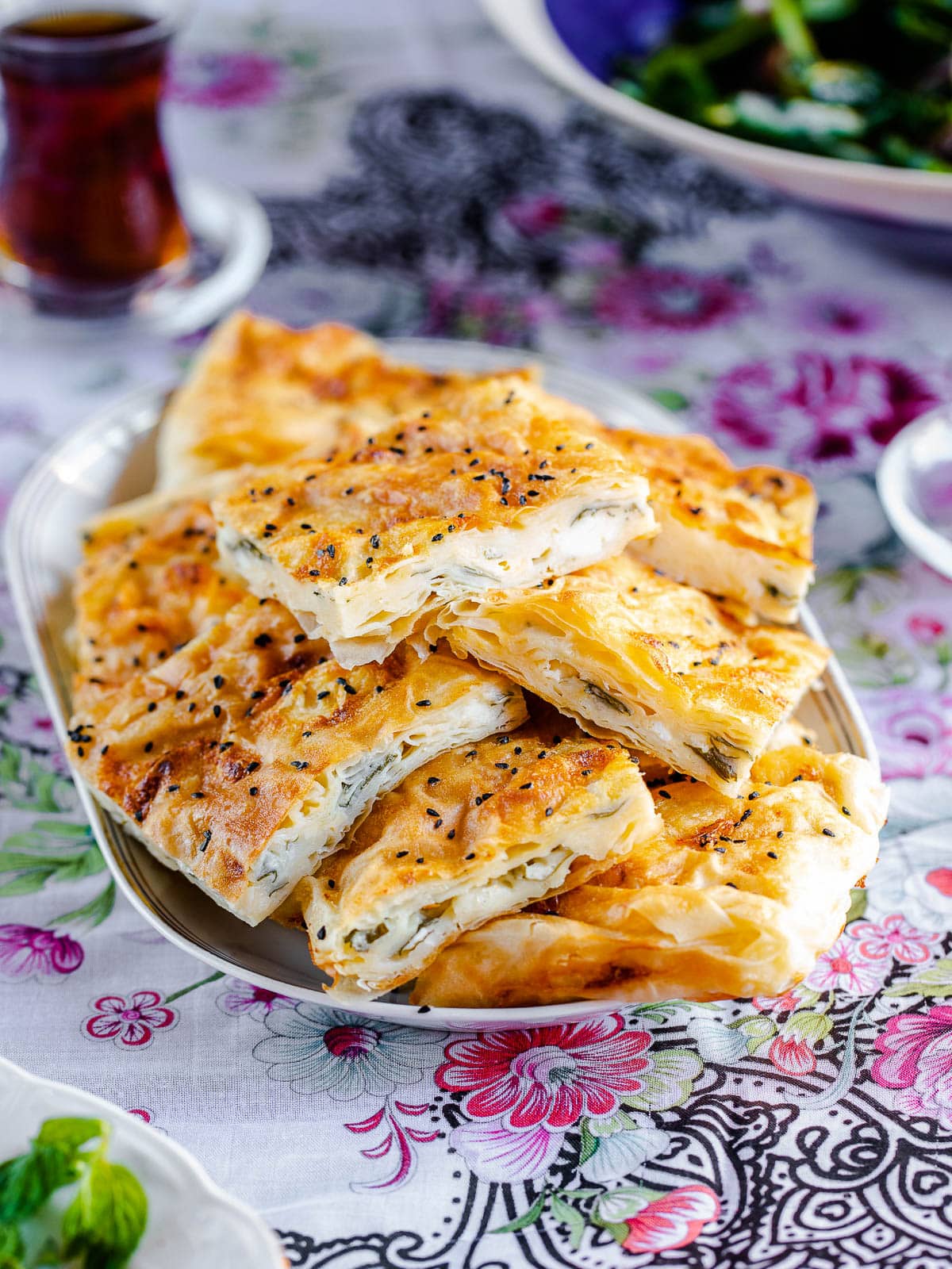 Plate stacked with Turkish tray börek on a rose patterned table cloth, seen from eye level