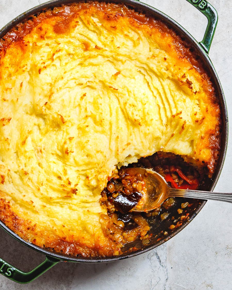 Vegetarian shepherd's pie with golden crust and a spoon having taken out a portion, making the ragu visible, seen from above