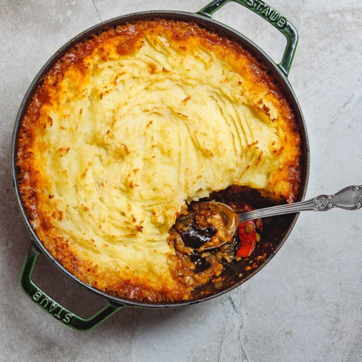 Vegetarian shepherd's pie with golden crust and a spoon having taken out a portion, making the ragu visible, seen from above