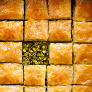 Baklava squares seen from above, with the top taken off one piece to show the green pistachio filling.