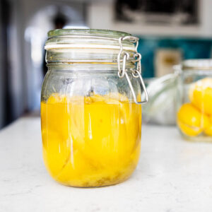 Homemade preserved lemons in a jar on marble countertop, seen from the side