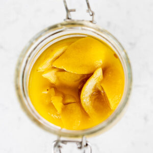 Homemade preserved lemons in a jar on marble countertop, seen from above