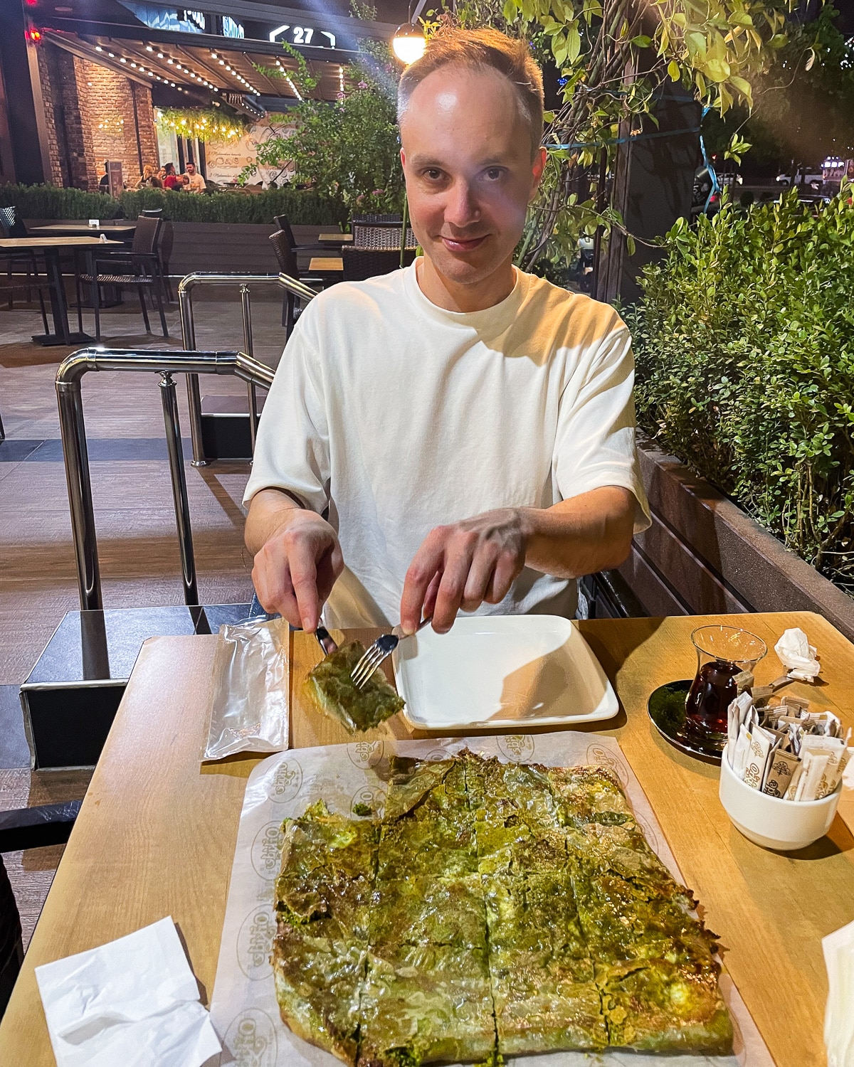 A huge katmer on a cafe table in Gaziantep, with Vidar about to tuck in. The katmer is large and completely green from all the pistachios it's stuffed with.