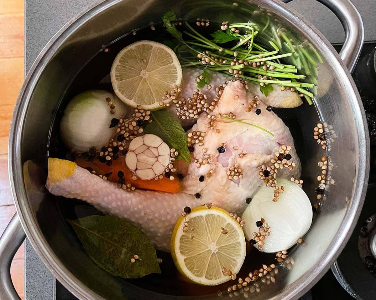 Stock pot with chicken and vegetables in water, seen from above.