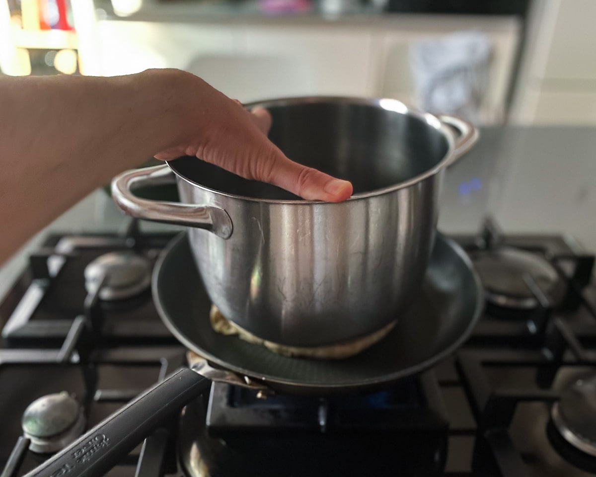 A hand is pressing an empty pot sitting on top of an arayes in a hot pan.