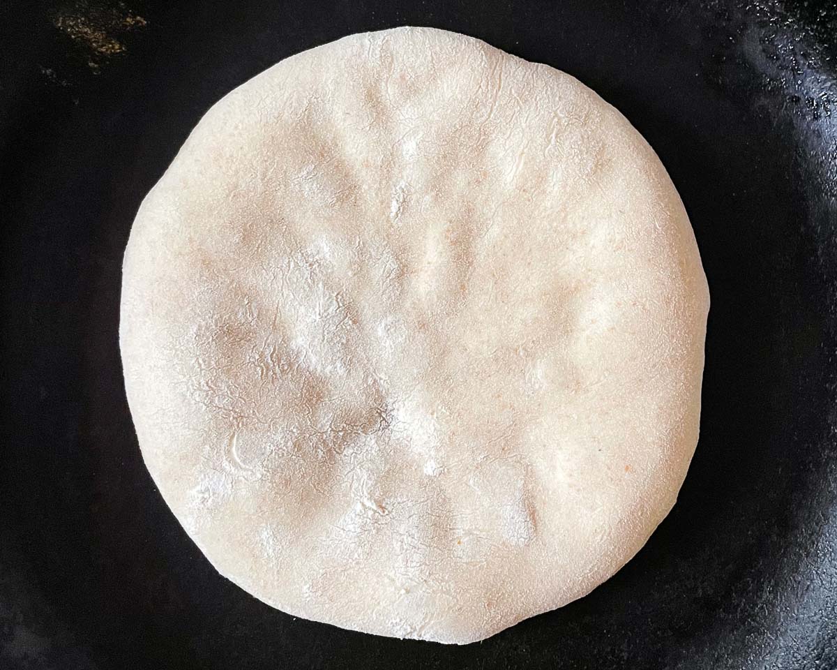 A bazlama frying in a black pan, not yet fried side up