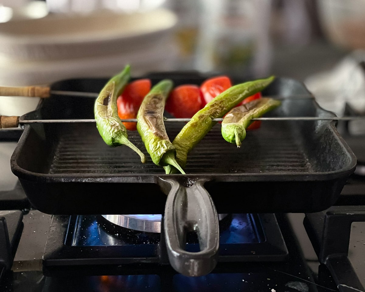 Green peppers and tomatoes grilling on a skewer over a very hot grill pan. The gas flame is visible underneath the pan