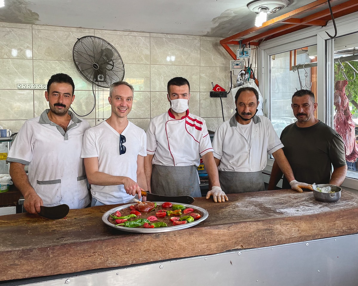 Vidar Bergum posing behind a tepsikebab together with a few butchers dressed in white. Vidar is holding a traditional zirh knife, which is large and slightly curved.