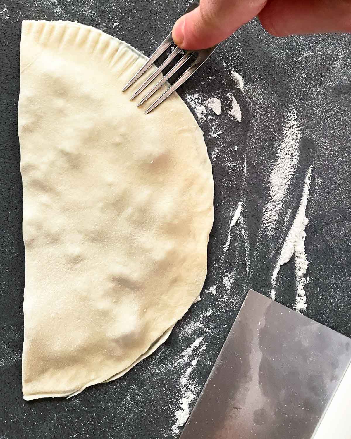 A fork is pressing down the edges of a chebureki before frying.