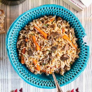 Uzbek plov in a turqouise dish on a patterned table cloth.