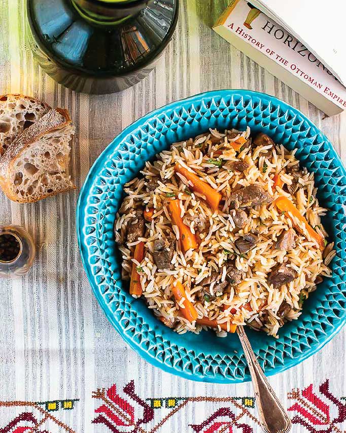 Uzbek plov in a turqouise dish on a patterned table cloth.